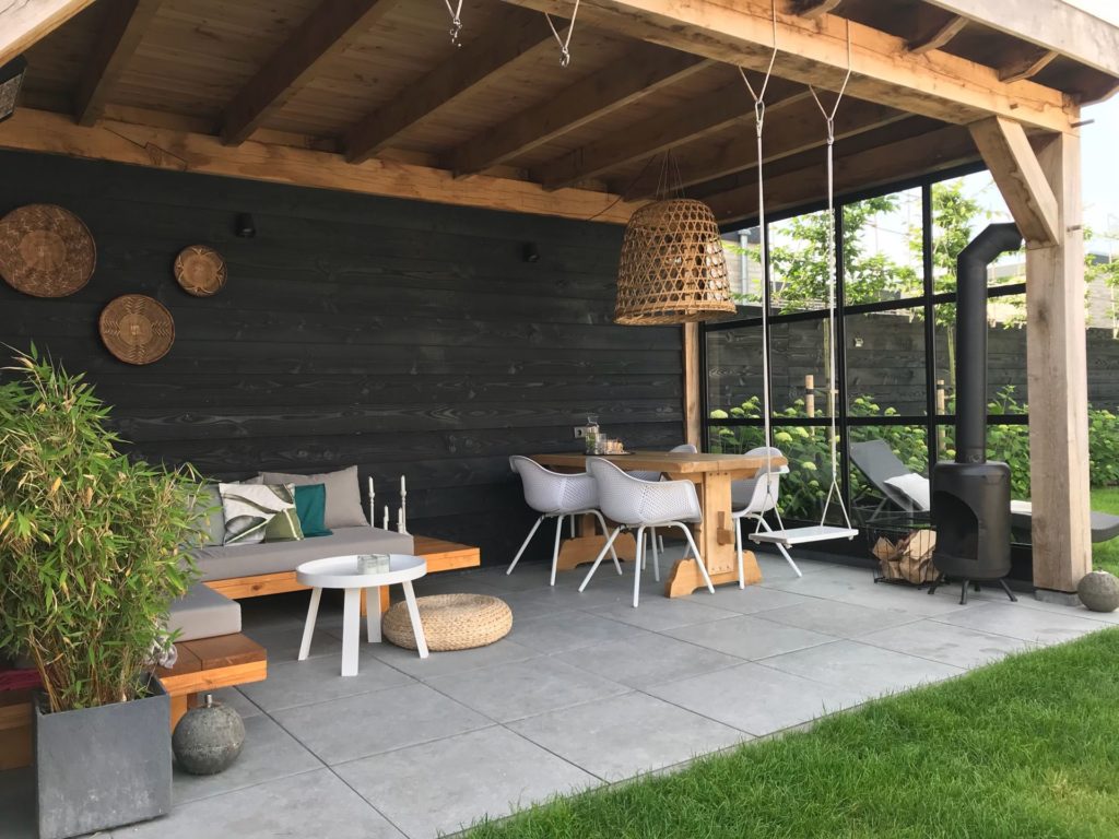 moderne tuin idee voor een grote houten overkappen met daaronder een loungeplek met loungeset, tuinset en een tuinhaard